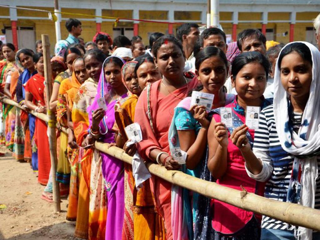 Women voters stand in line displaying their voter ID cards outside a polling booth in Bihar. The Election Commission has permitted 12 alternative ID proofs for the 2025 Assembly polls, with special provisions for purdanasheen women to ensure inclusive participation. (The Hindu)
